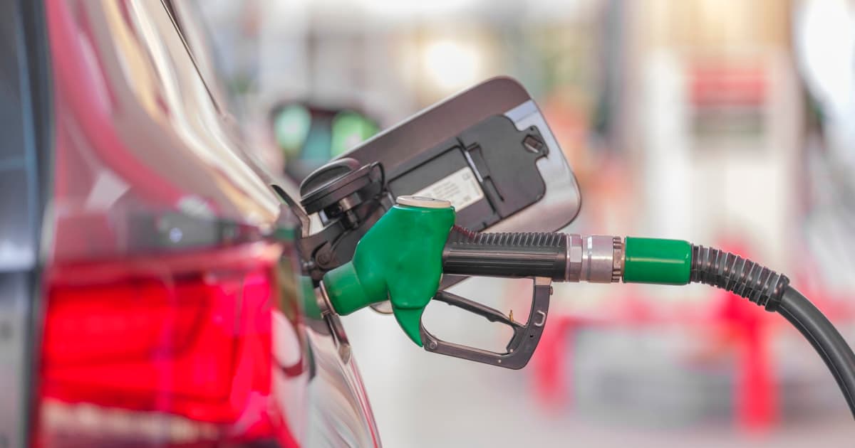 A green fuel nozzle pumping gas into a car at a station — gas prices by state, 2026